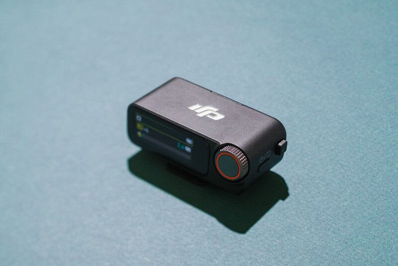 Compact action camera with black body and orange accent ring on turquoise surface.