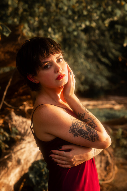 Woman with shoulder tattoo posing against textured golden backdrop in studio lighting.