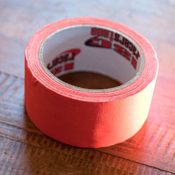 Roll of bright red packing tape positioned on a wooden surface with blurred background.