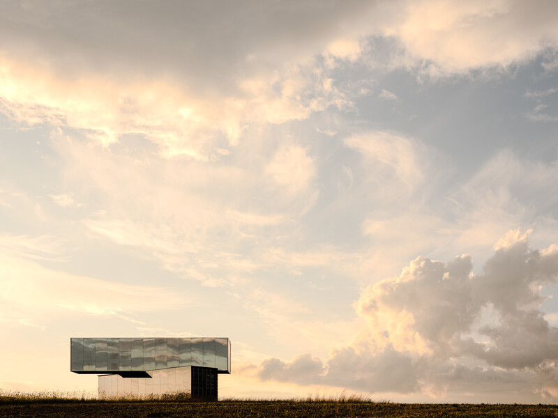 Minimalist landscape with a single billboard structure on flat terrain beneath dramatic cloudy sky.