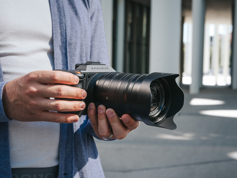 Photographer holding a telephoto lens with a lens hood attached, wearing casual clothing indoors.