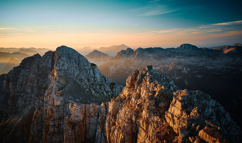 Rocky mountain peaks bathed in golden sunrise light with misty valleys below.