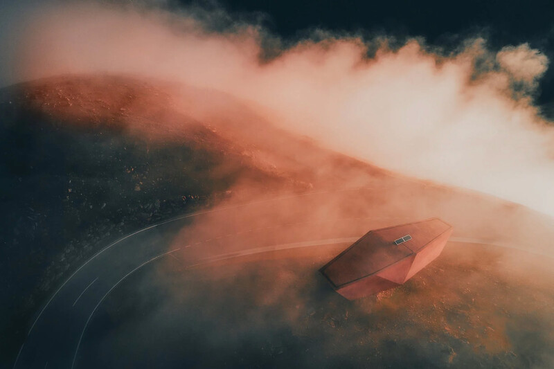 Aerial view of a red car driving on a winding road through misty, mountainous terrain.