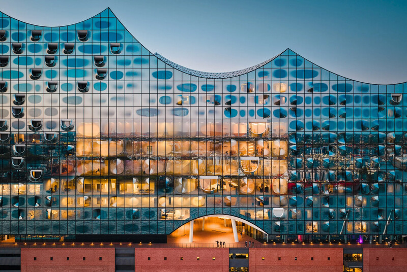 Modern glass building with undulating curved facade and circular window patterns, illuminated by golden hour light.