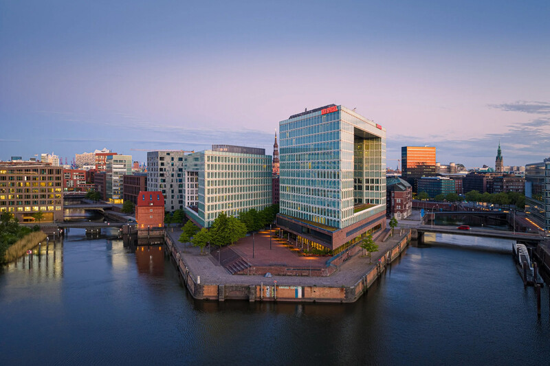 Modern waterfront cityscape at twilight with glass and brick buildings reflected in calm canal water.