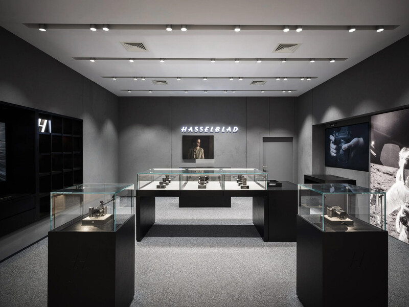 Modern luxury retail showroom with black display cases, recessed ceiling lights, and gray walls featuring product displays.
