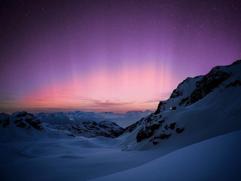 Snow-covered mountain valley at twilight beneath a purple and pink sky with stars visible.