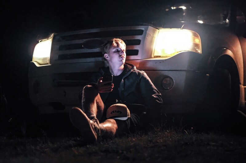 Person crouched in front of an illuminated vehicle at night, lit by the truck's headlights.