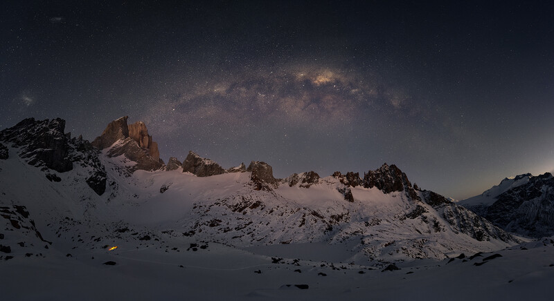 Snow-covered mountain peaks beneath a starry night sky with the Milky Way visible overhead.