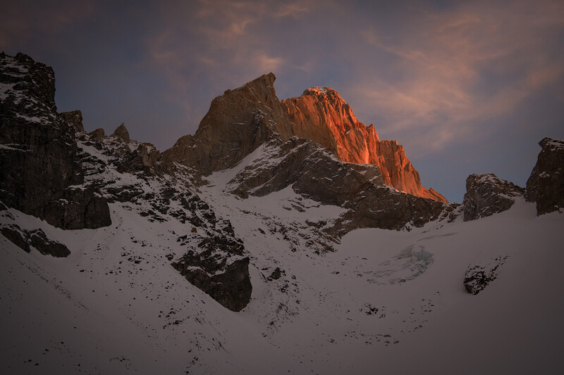Snow-covered alpine peaks with golden sunlight illuminating vertical rock formations at sunset.