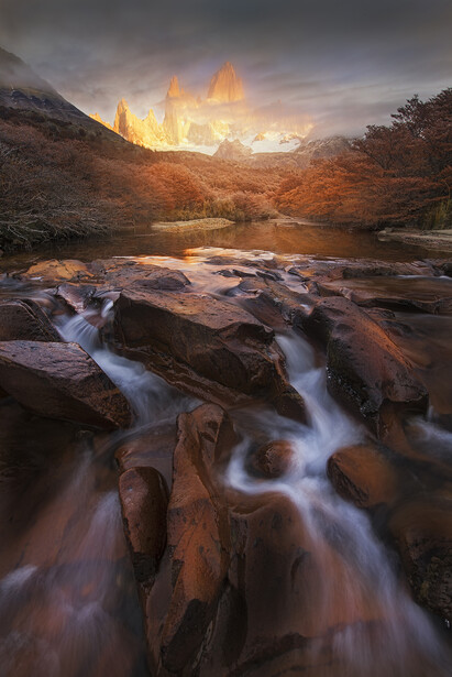 Long exposure photograph of a flowing mountain stream with golden-hour light illuminating distant peaks.
