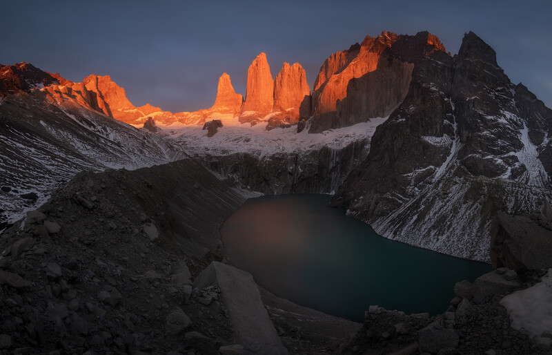Alpine lake surrounded by granite peaks with golden sunrise light illuminating distant towers.
