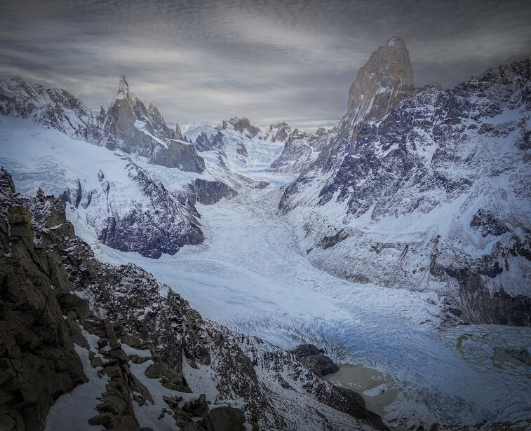 Snow-covered alpine peaks and glaciers under overcast skies in a high mountain range.