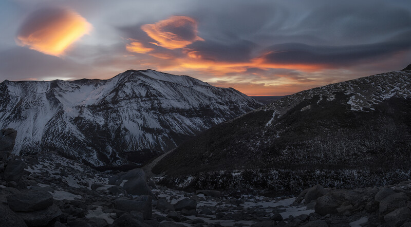 Snow-covered mountains at sunset with dramatic golden and orange clouds illuminating the sky.
