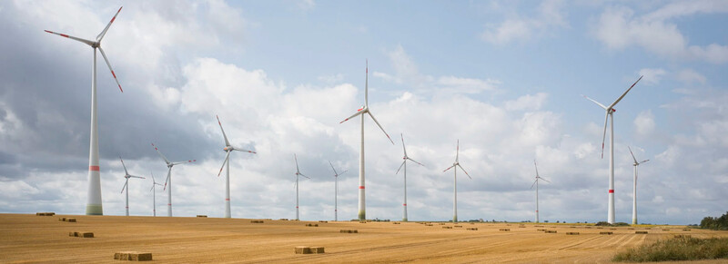 Multiple wind turbines scattered across a harvested grain field under a partly cloudy sky.