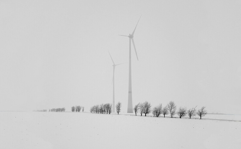 Wind turbines and bare trees in a snow-covered landscape under overcast sky.