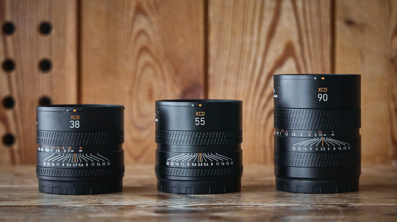 Three black telephoto lenses with focal lengths of 38mm, 55mm, and 90mm arranged in order of increasing size on a wooden surface.
