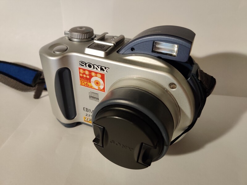 Sony Cyber-shot digital camera in silver and black, shown from above with lens cap attached and blue strap visible.