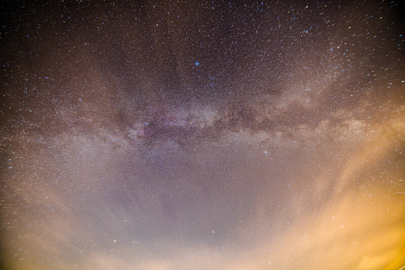 Milky Way galaxy stretches across night sky with purple and gold atmospheric glow.