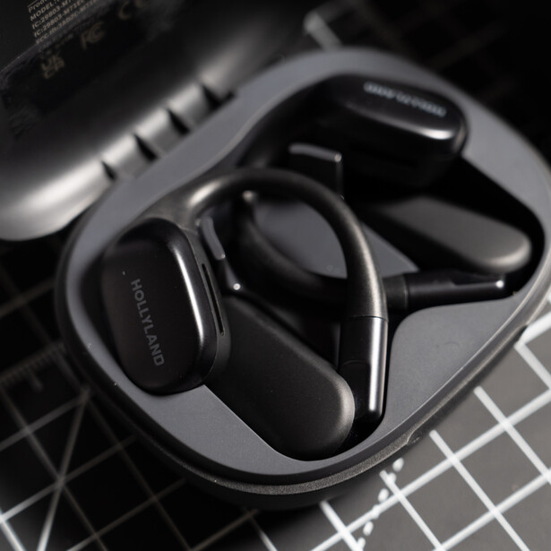 Wireless headphones resting in a charging case on a gridded surface, photographed in monochrome.