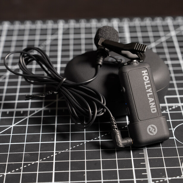 Wireless lavalier microphone with receiver unit and coiled cable on graph paper.