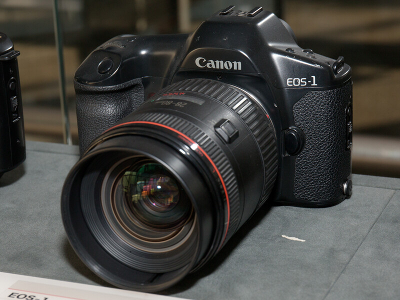 Canon EOS-1 DSLR camera with attached zoom lens displayed on a gray surface.