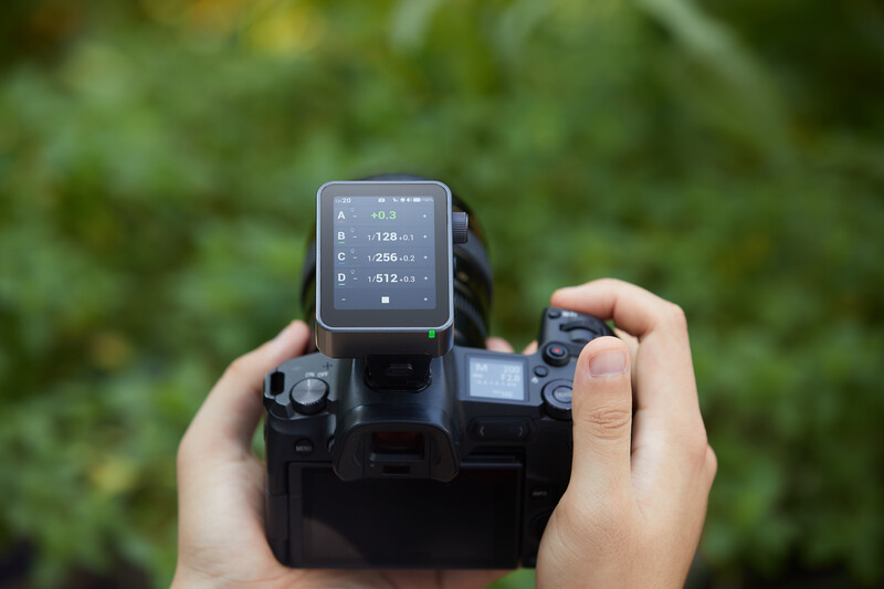 Photographer holding a camera with a small digital display screen mounted on top against a blurred green background.