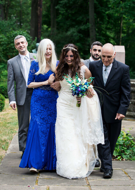 Bride and groom walking with wedding party members through a tree-lined path.