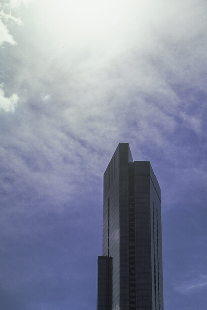 Modern skyscraper shot from below against a dramatic blue sky with wispy clouds.