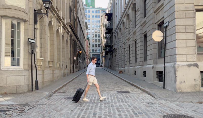 Man pulling a rolling suitcase while walking down a narrow European cobblestone street lined with classical stone buildings.