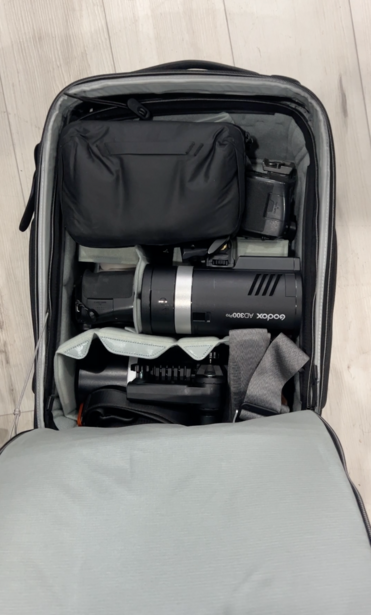 Open camera backpack displaying organized photography gear including a mirrorless camera, lenses, and accessories in compartments.