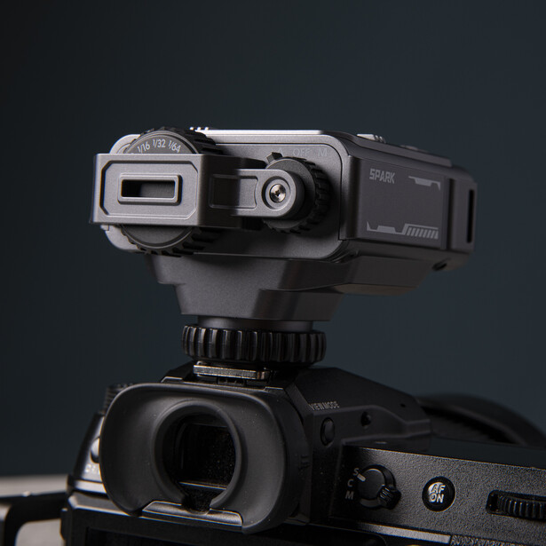 Compact video camera with articulating screen mounted on DSLR camera body against dark background.