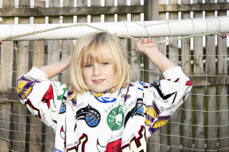 Young child with blonde hair smiling at camera while holding a horizontal pipe above their head.