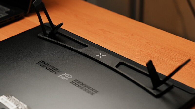 Black monitor arm mounted on orange wooden desk with adjustment controls visible.