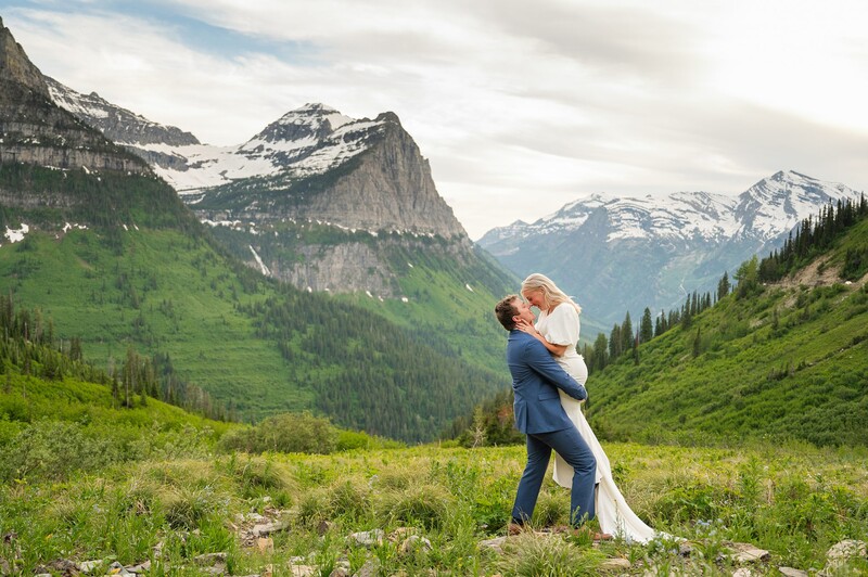Groom lifting bride in a valley meadow with snow-capped mountains in the background.