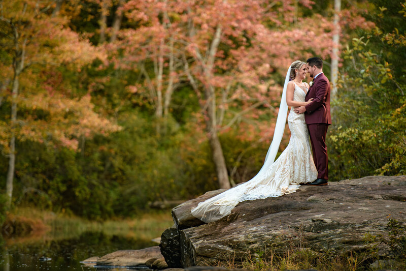 Bride and groom kissing on a rocky outcrop beside a river, bride's veil flowing dramatically behind them.