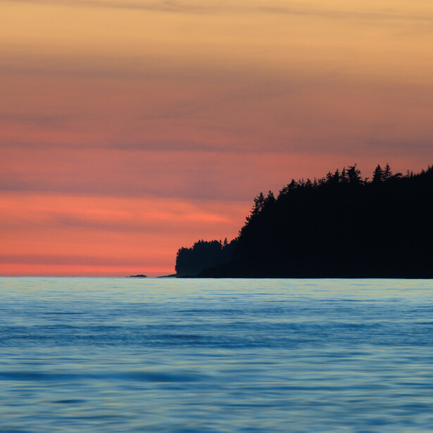 Photograph of sunset colors and long exposure ocean surrounding a silhouetted headland