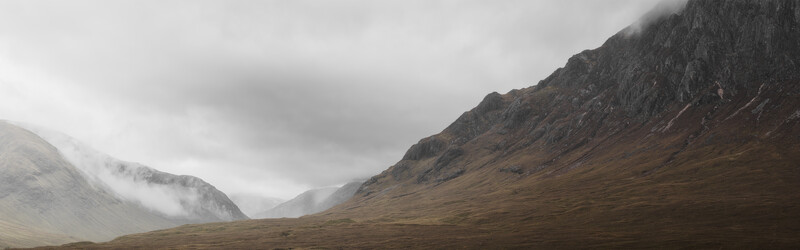 Alpine valley with barren mountains under overcast sky, mist rising from distant peaks.
