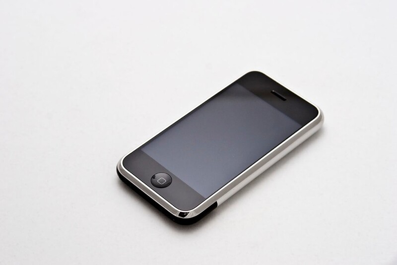 Early-generation smartphone with dark screen displayed at an angle on light gray surface.