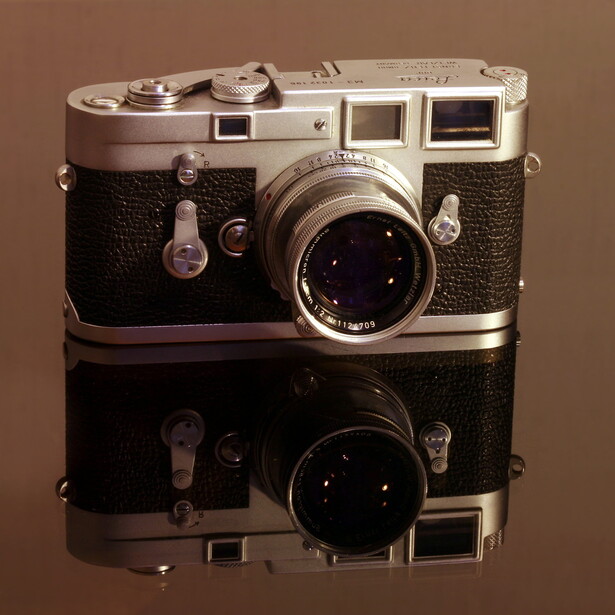 Vintage rangefinder camera with chrome and black leather body, shown from above with its reflection on a reflective surface.