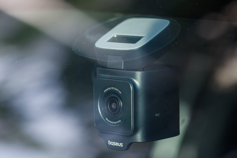 Baseus car dash camera mounted on windshield with display screen visible and blurred background.