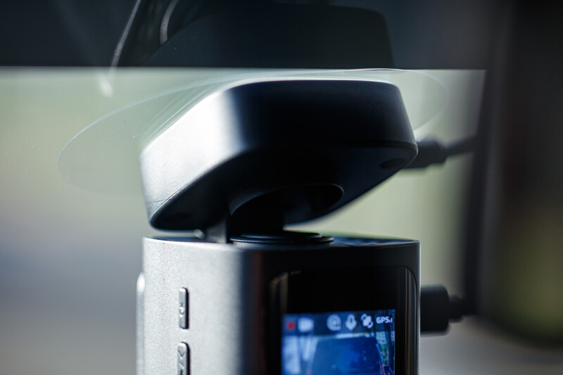 Close-up of a compact camera or action camera with lens cap open, showing LCD screen with blue interface elements.