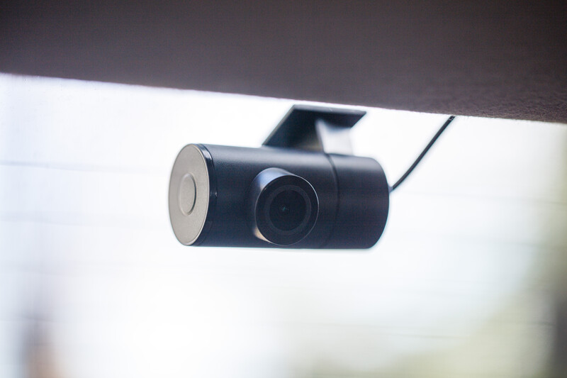 Black dash camera mounted on vehicle windshield with power cord visible.