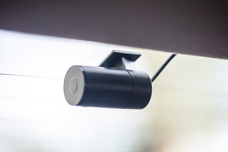 Compact cylindrical dashcam mounted on a white vehicle headliner with angled bracket.