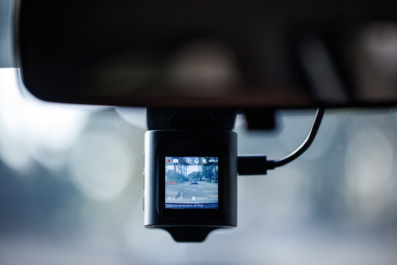 Dash cam mounted on a car windshield displaying a street scene on its small screen.