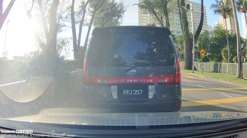 View from inside a car following a dark blue minivan with red taillights on a tree-lined suburban street.