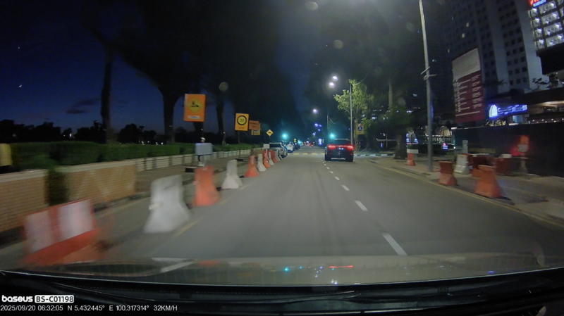 Dashcam footage of a nighttime urban street with construction barriers and high-rise buildings.