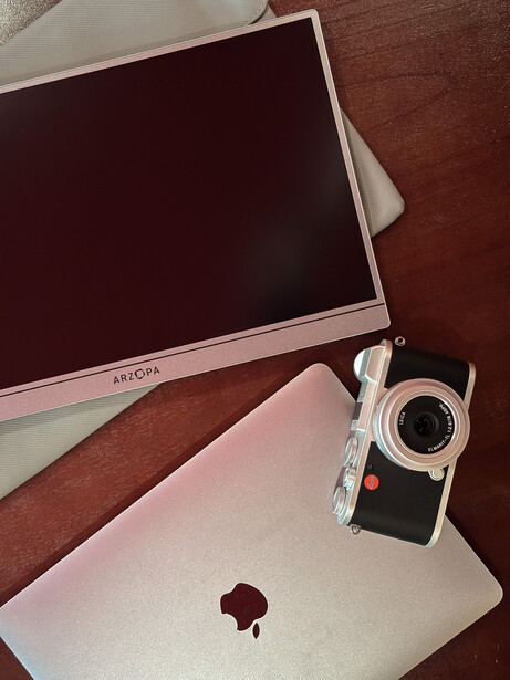 Pink laptop, monitor, and vintage film camera arranged on a wooden surface.