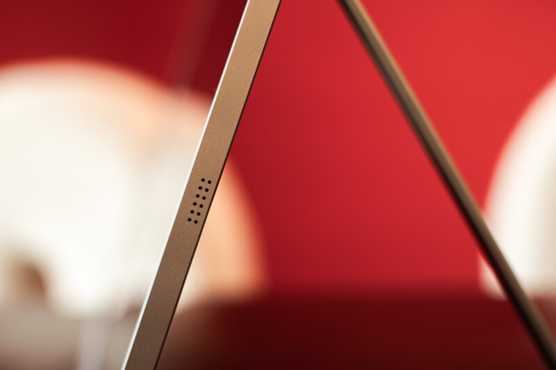 Close-up of a smartphone's edge showing speaker grille and antenna lines against a red blurred background.