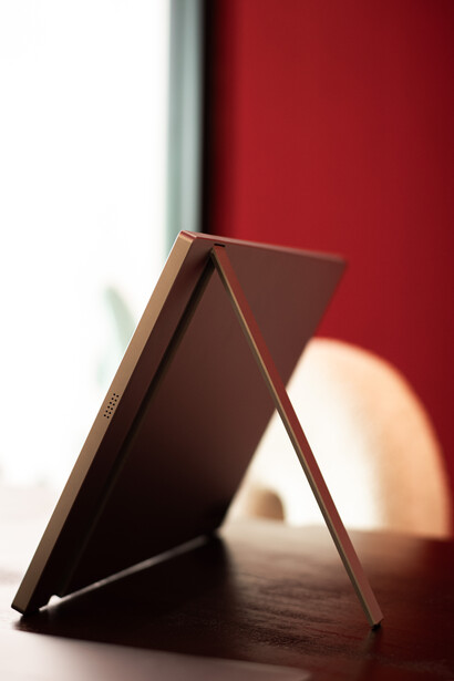 Wooden picture frame standing at an angle against a deep red wall with dramatic side lighting.